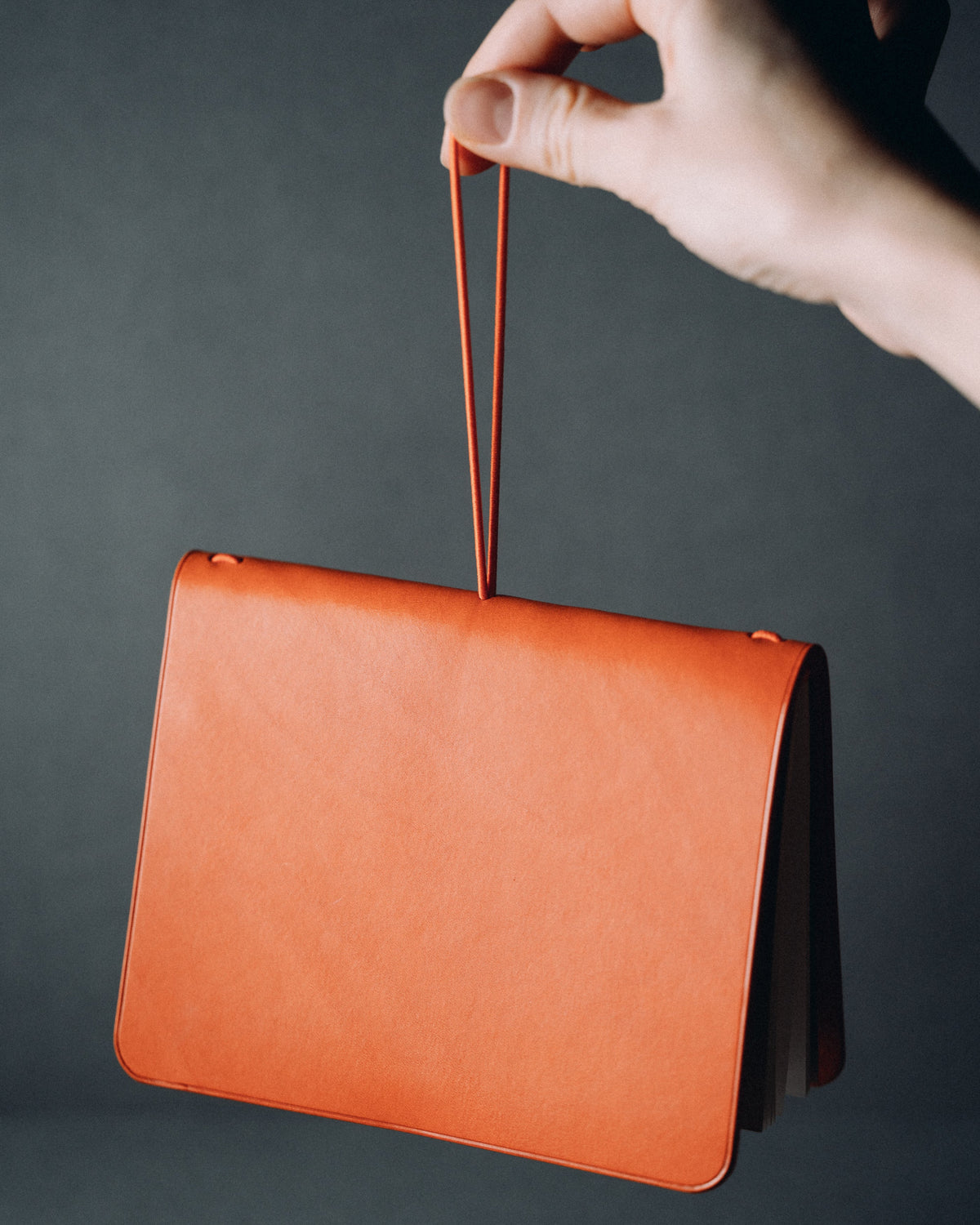 An orange leather notebook cover hanging from an elastic cord held in one hand.