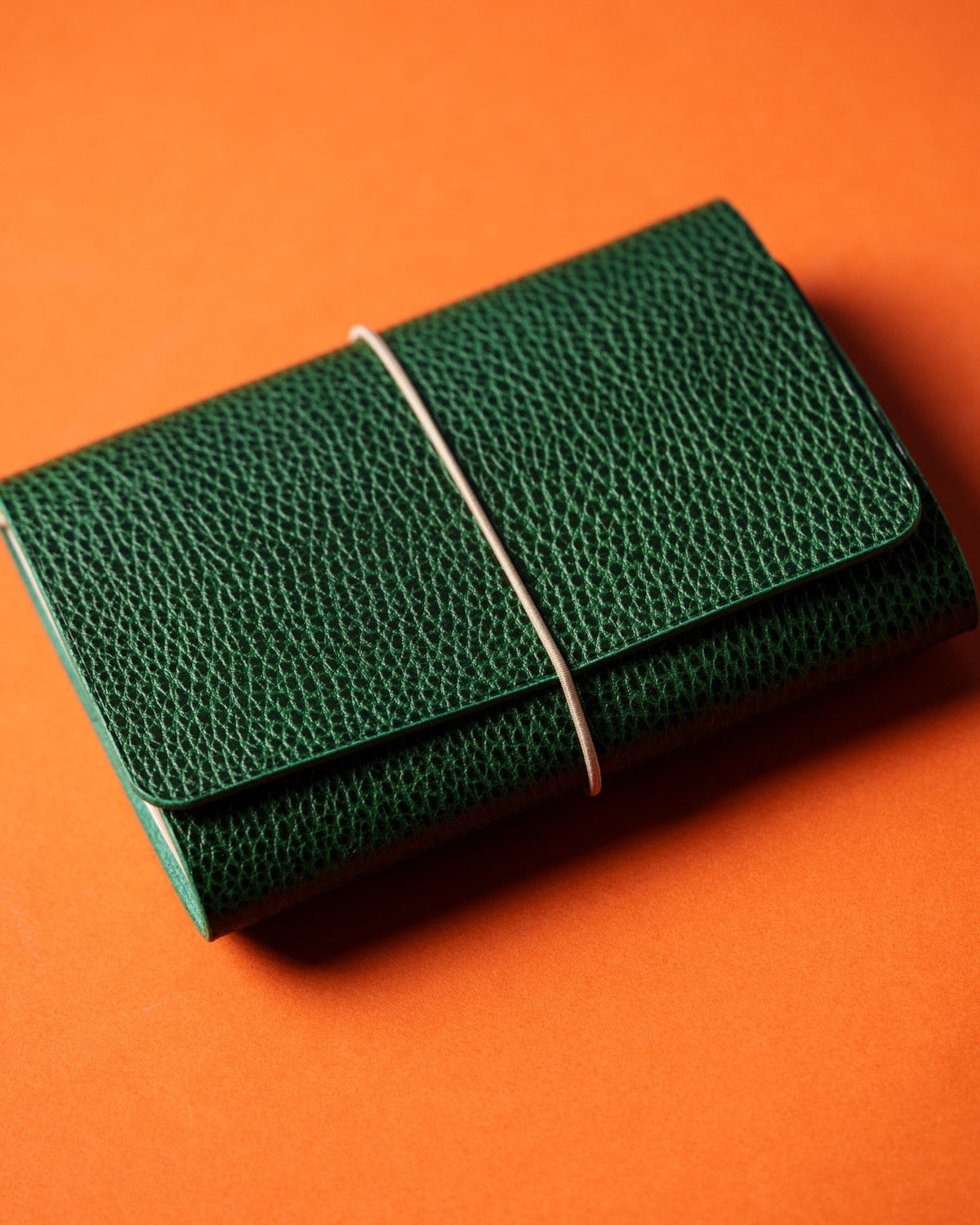 Green pebbled leather trifold cover closed with a pale elastic, on an orange background