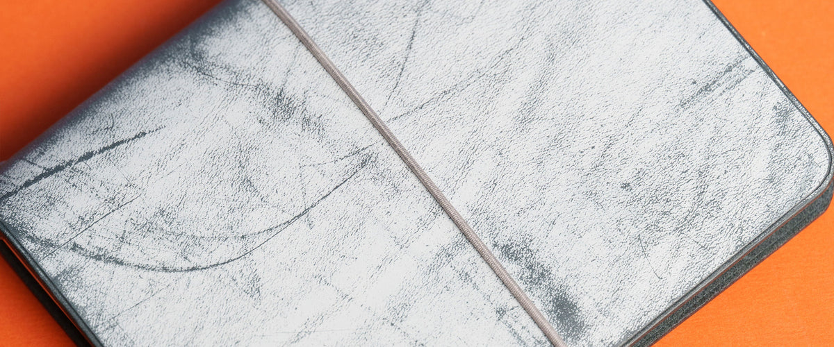 A close-up of pale wax patterns across dark leather, set against an orange background.