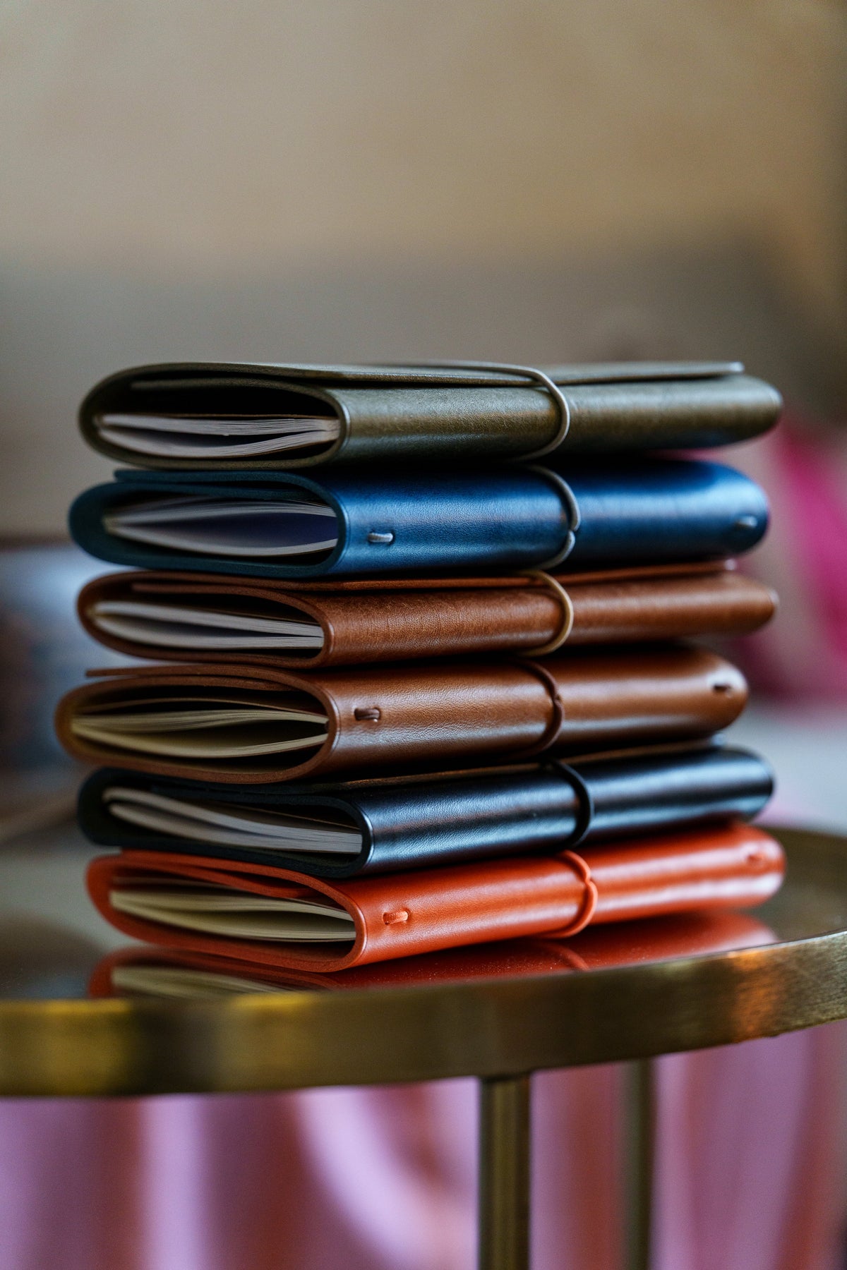 A stack of colourful leather-covered notebooks on a round side table in soft window light.