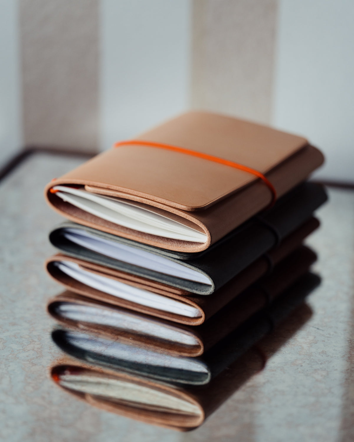 A stack of leather-covered notebooks reflected in a glossy tabletop beside a window.