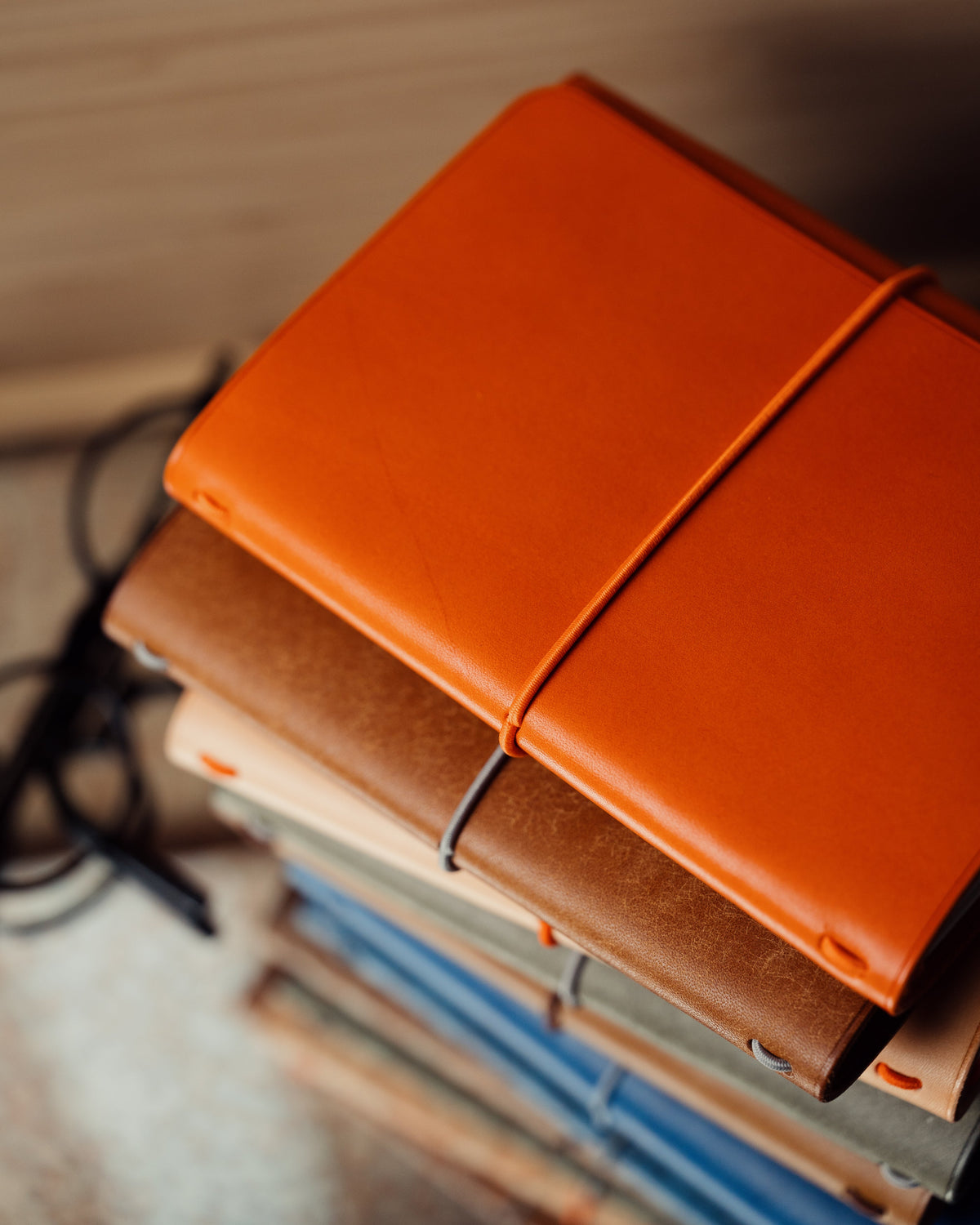 An orange leather-covered notebook on top of a stack, with glasses resting on the table beside it.