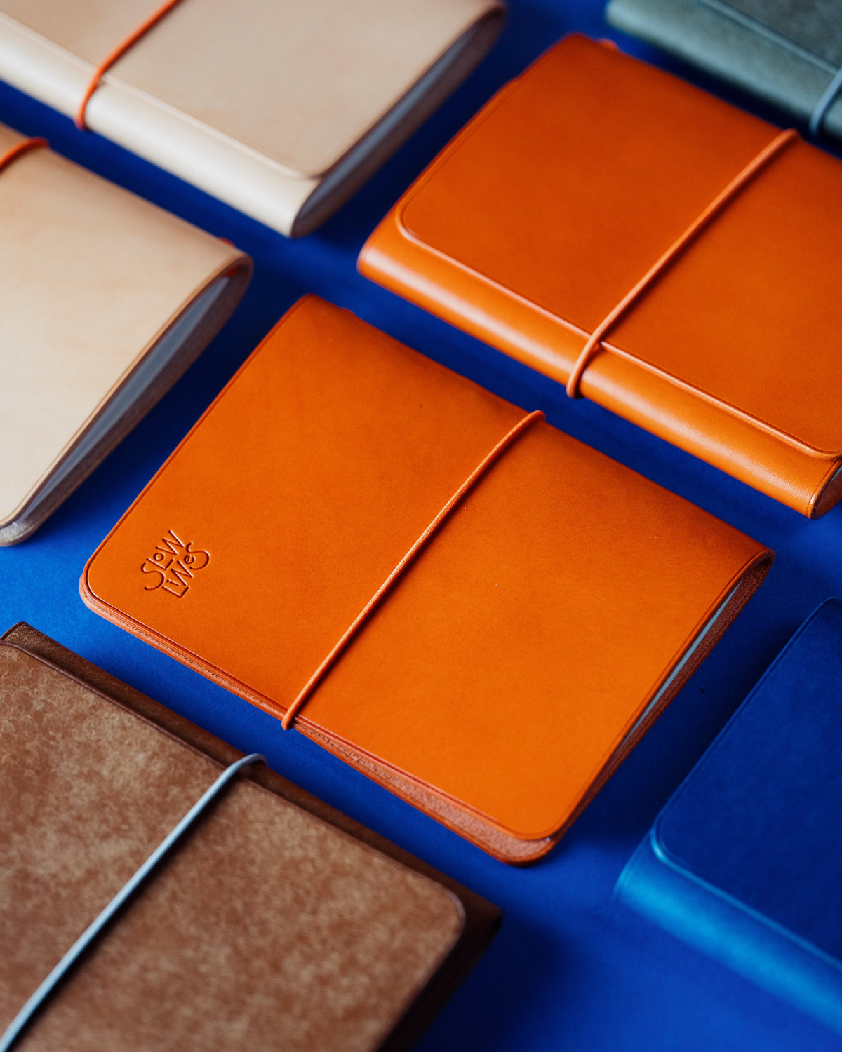 Leather notebook covers of different sizes arranged diagonally on a vivid blue background.