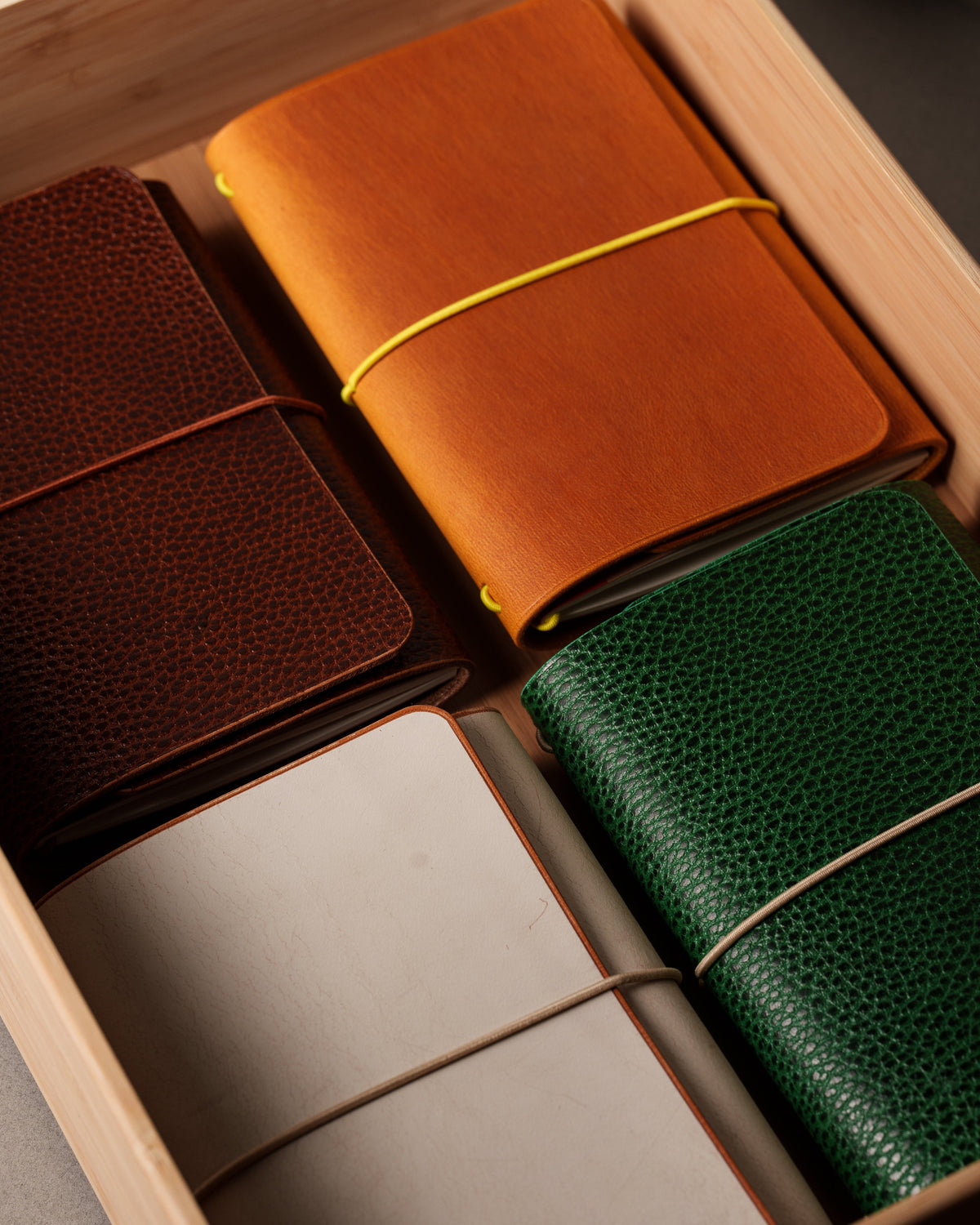 Orange, cream, brown and green leather notebook covers arranged in a wooden drawer.