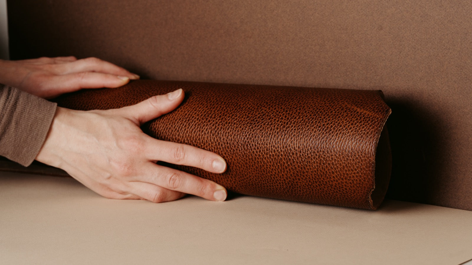 Hands rolling out a brown pebbled leather hide in the workshop