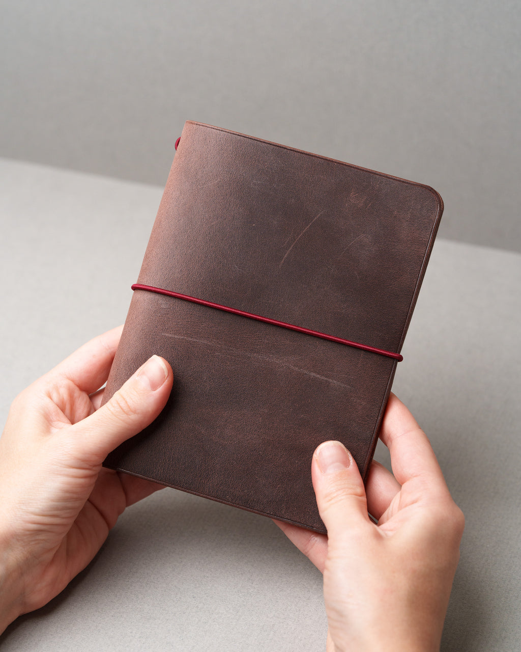 Brown Freedom Leather Cover, closed cover held in two hands, on grey