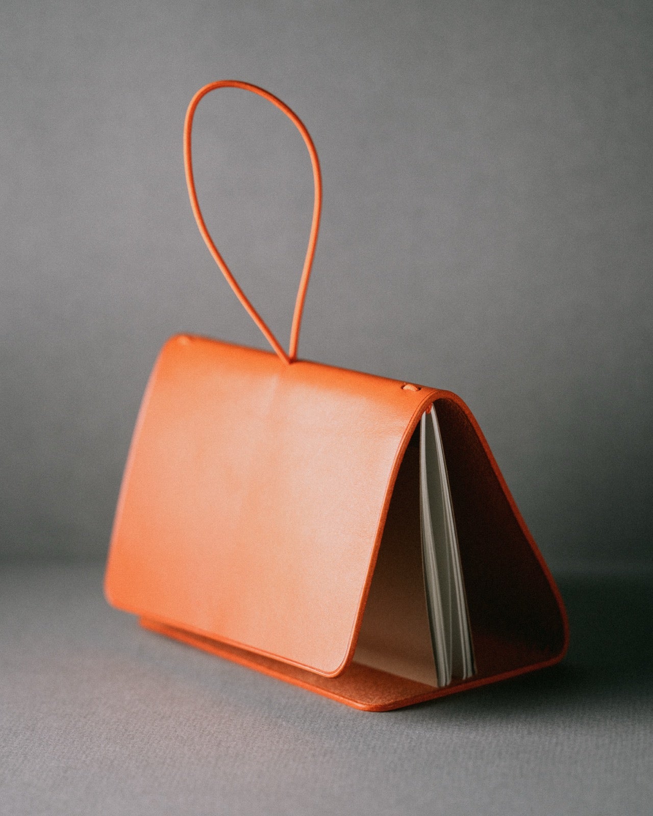 Orange leather trifold cover standing open, notebook block held inside by the elastic loop