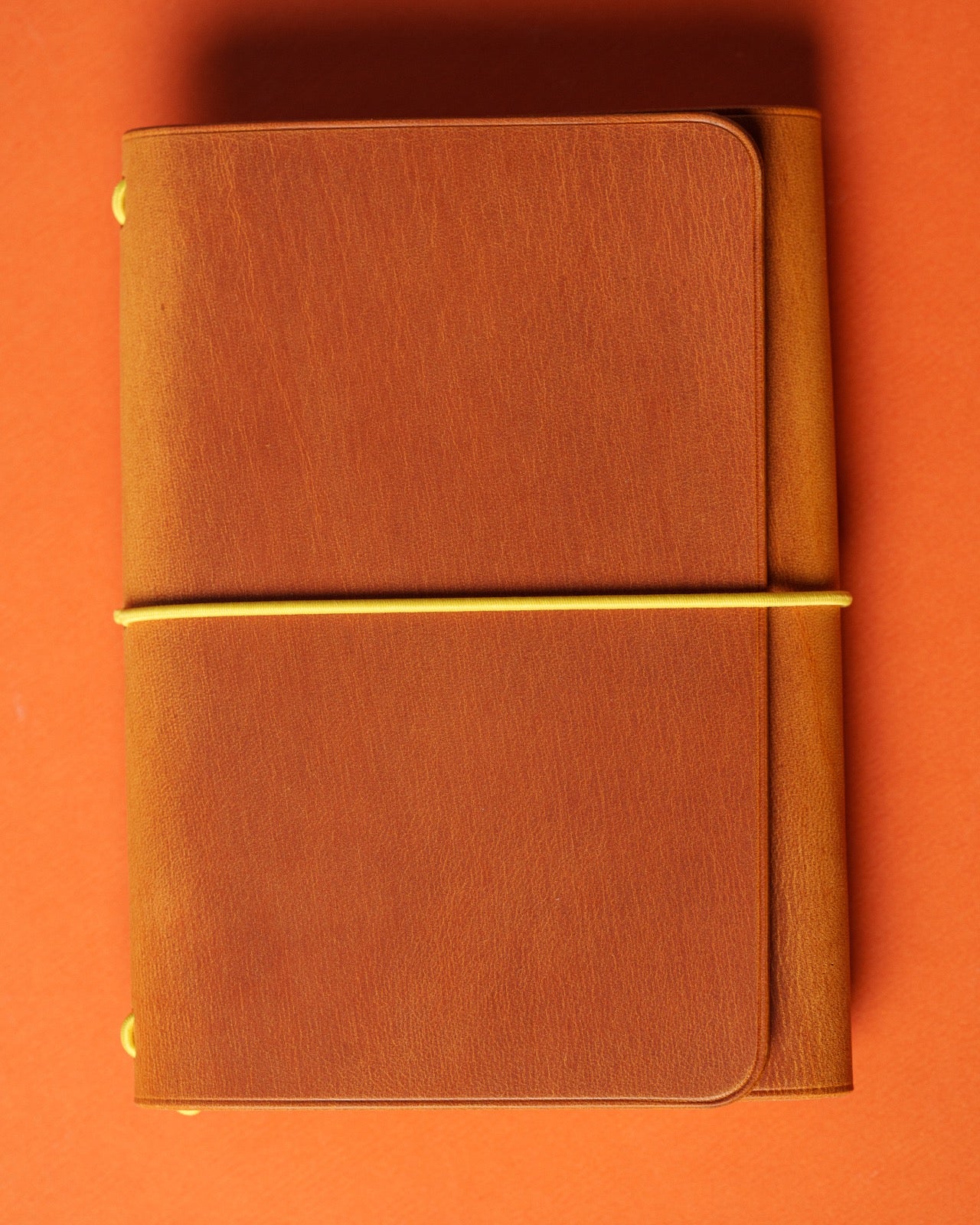 Light brown leather trifold cover closed with a yellow elastic across the front