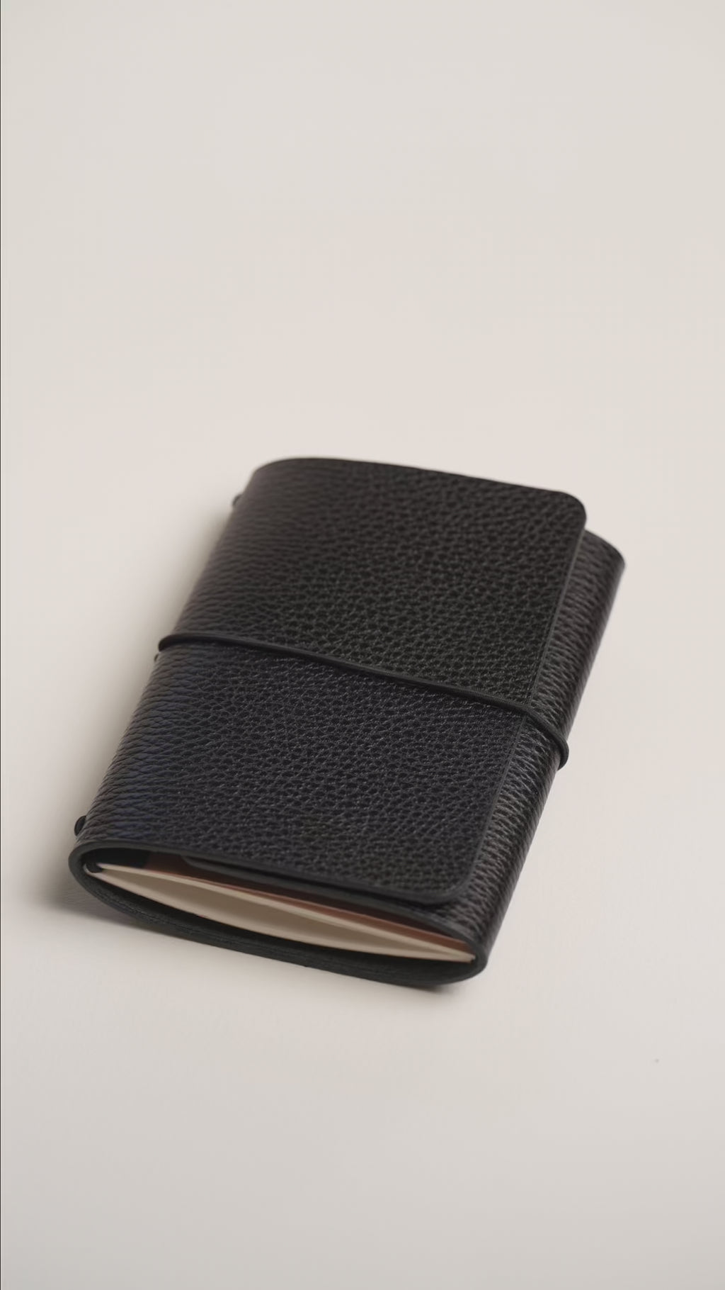 Hands opening the Black Dollaro trifold notebook trifold: elastic closure, vegetable tanned leather and the interior with the notebook in place.