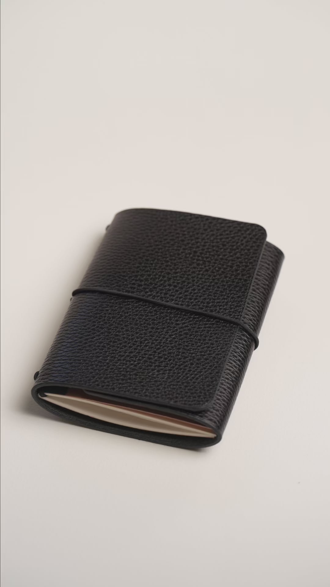 Hands opening the Black Dollaro trifold notebook trifold: elastic closure, vegetable tanned leather and the interior with the notebook in place.